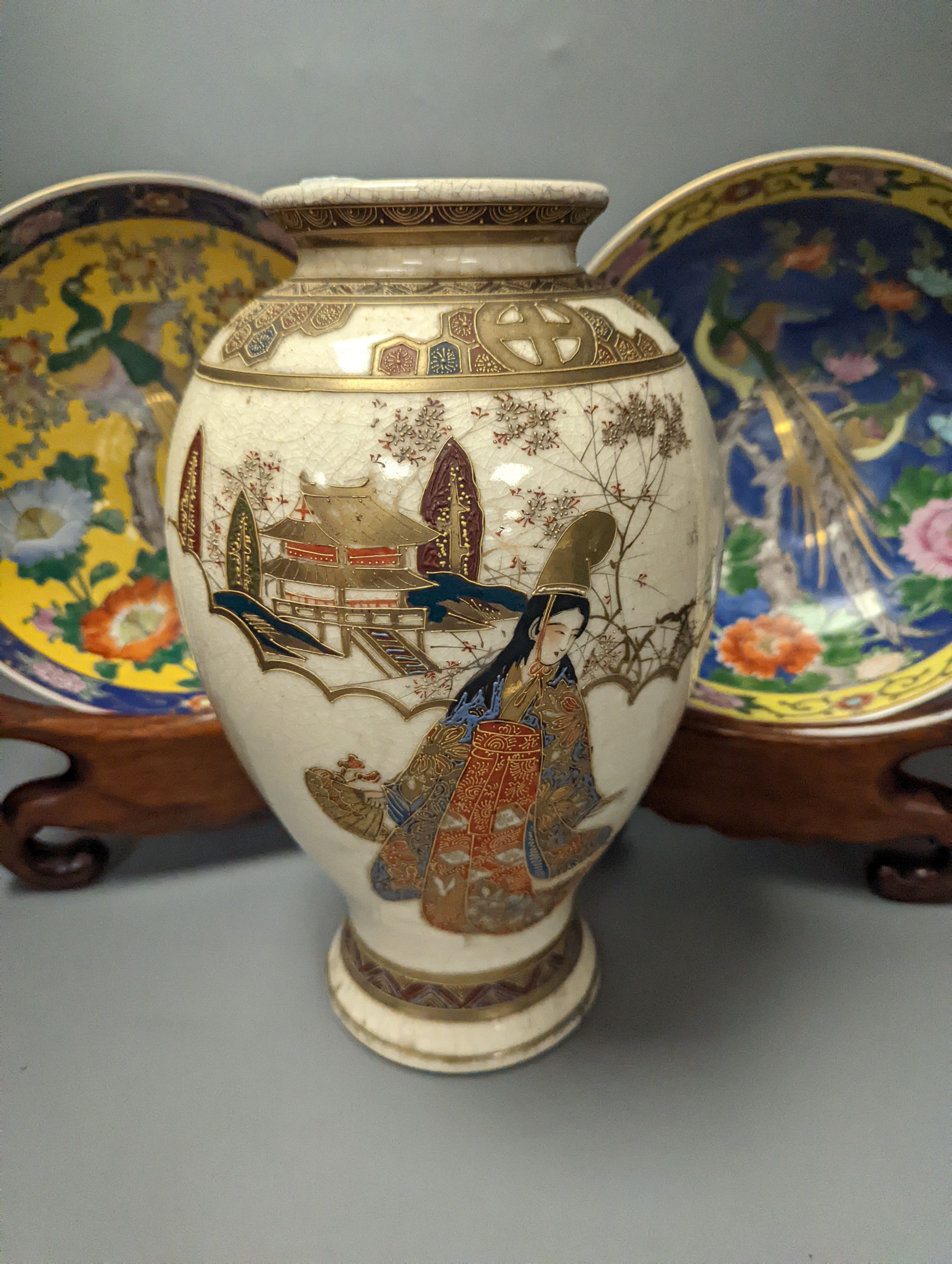 A Japanese Satsuma vase of a geisha and two Japanese yellow and a blue ground bowls each on wooden stands, Stands 32 cms high x 26cms deep.